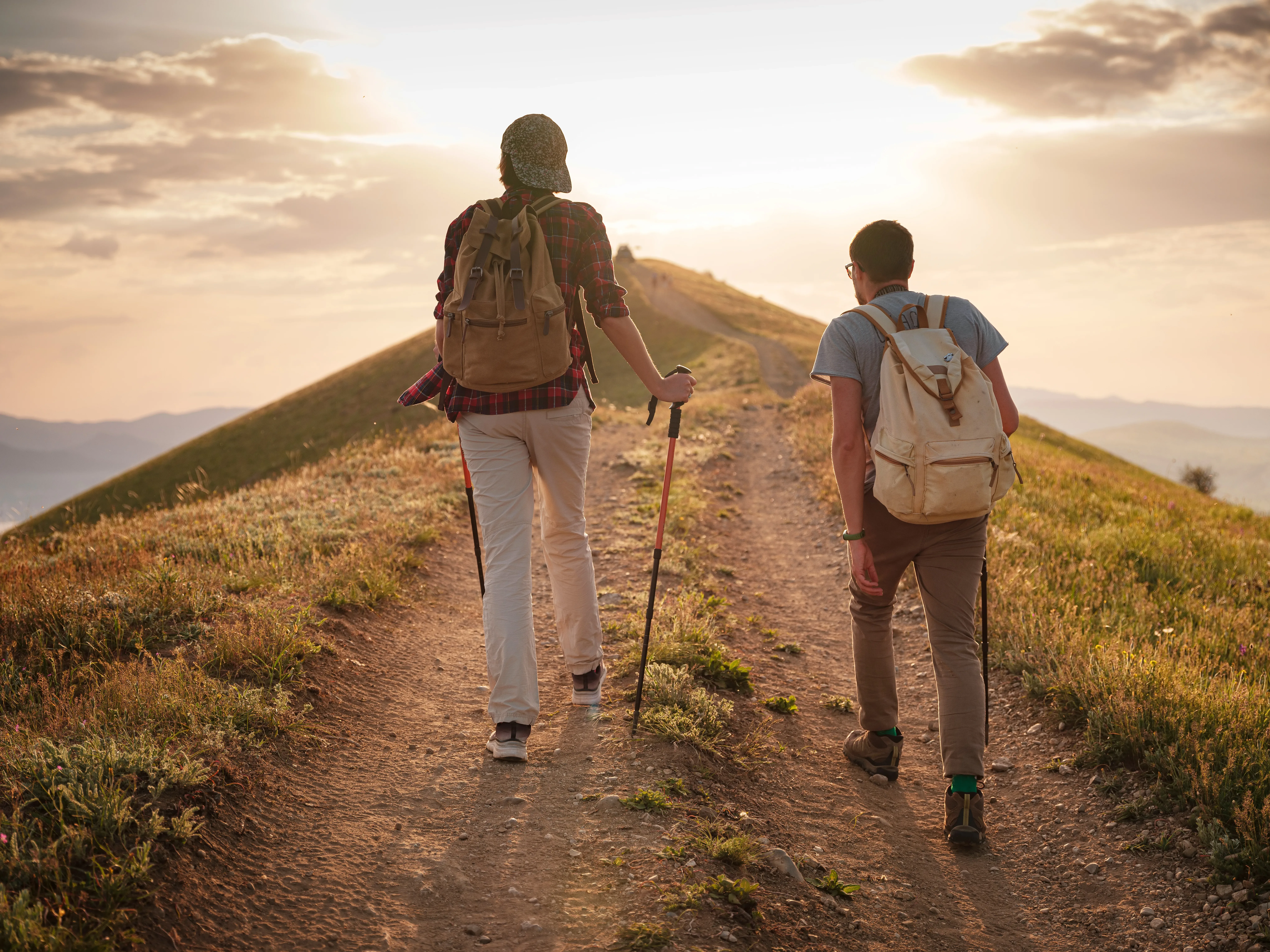 A couple of happy young hikers backpacking on a beautiful rocky trail on a warm, sunset evening. The concept of family travel and adventure. view from behind. Travel lifestyle.
