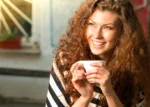 A smiling woman with curly brown hair holds a coffee mug