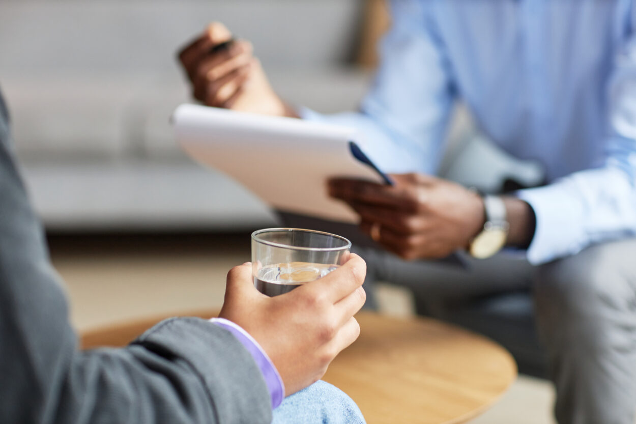 Hand of teenage boy squeezing glass of water when talking to adolescent psychologist