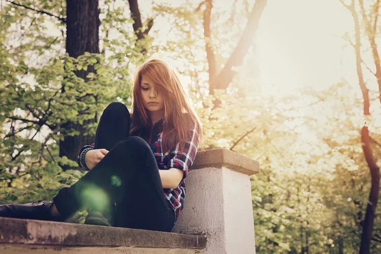 a depressed teen sits on a park bench