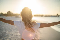 Cheerful young woman embracing nature at sunset; female standing on beach arms outstretched, Cancun, Mexico