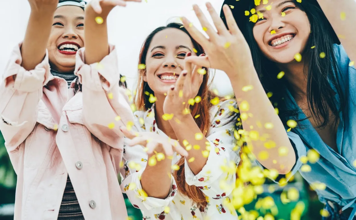 Group of female friends smiling while tossing flower petals in the air
