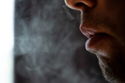 Male lips blowing smoke close-up, cigarette smoke and lips on black background, male unshaven and short beard.