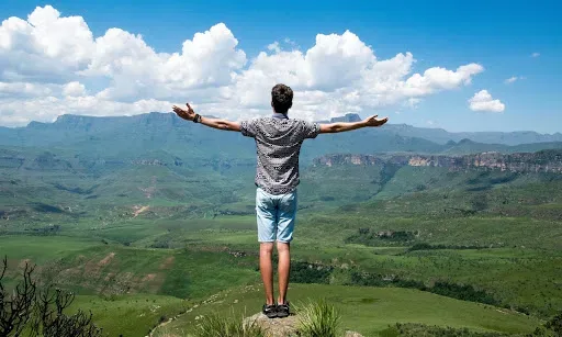 Man Standing on a rock overlooking a valley with his arms spread wide