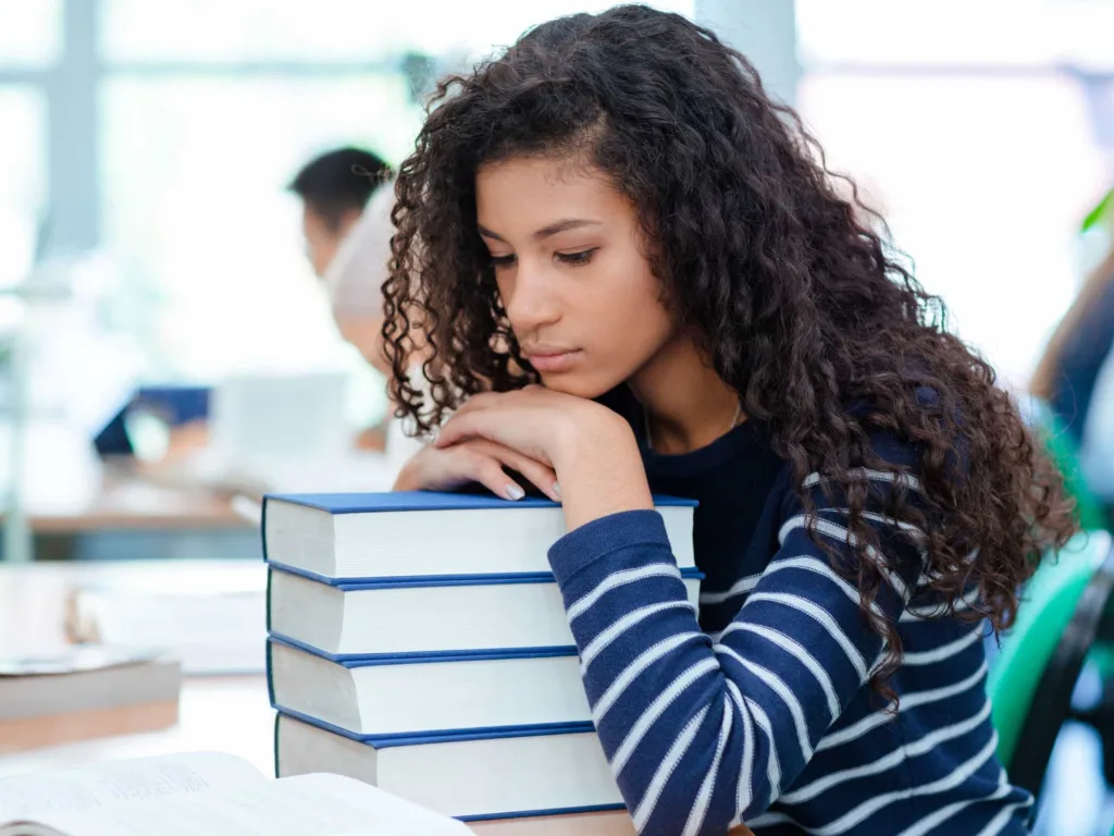 A female college student slumps over a pile of books