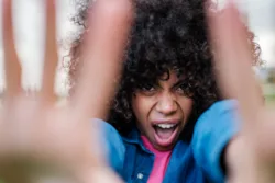 Curly-haired woman screaming at the camera and covering it with her hands