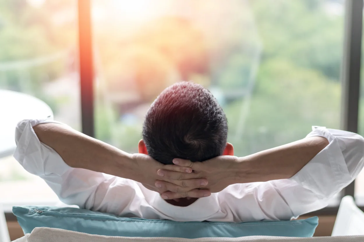Good life and easy relax business man lifestyle after work from home sitting hands behind head for happy businessmen people. Work life balance concept.