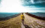 Hiker with backpack hiking on the top of a mountain - Man walking on forest path at sunset - Focus on the guy