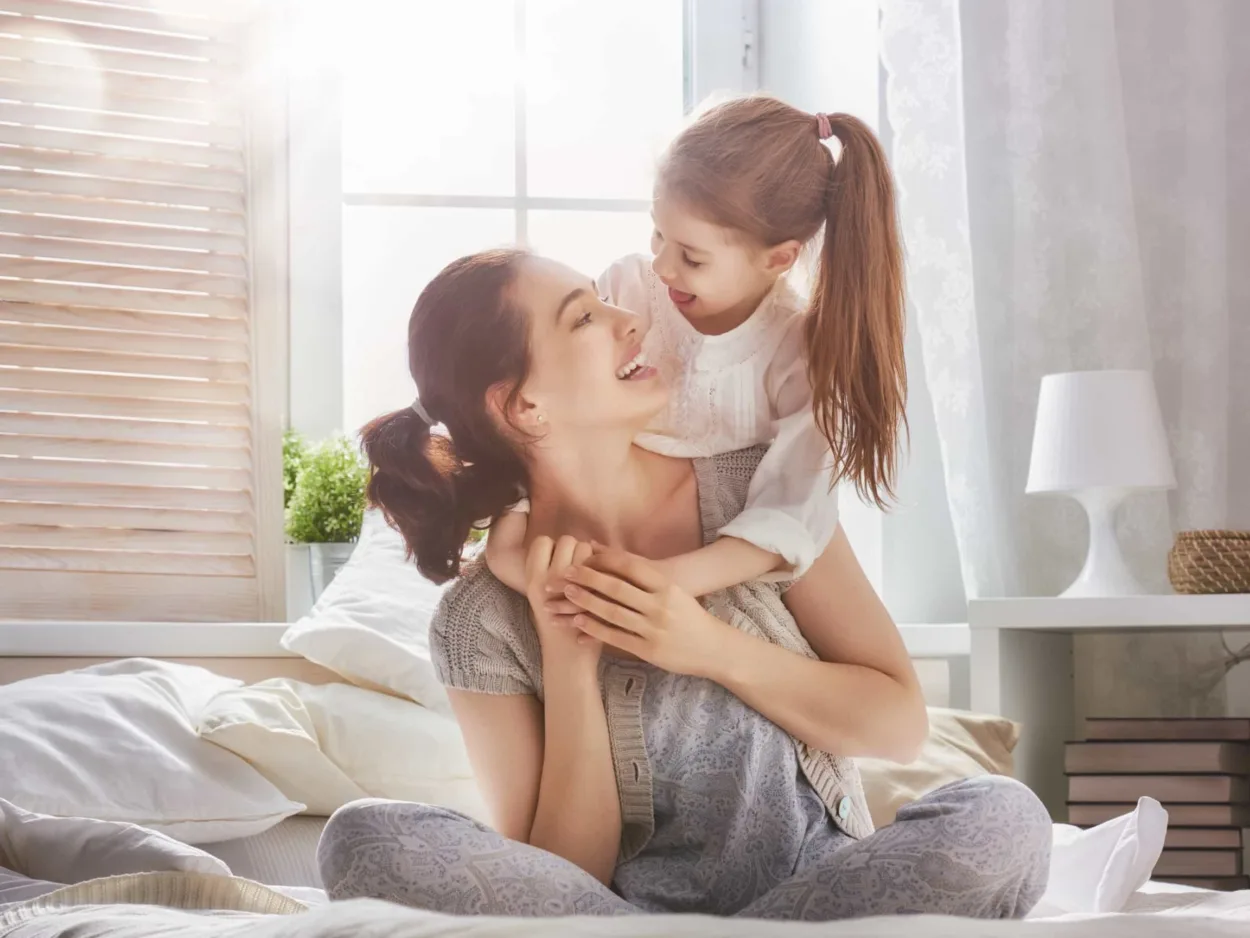 A mother and her daughter sit on a bed