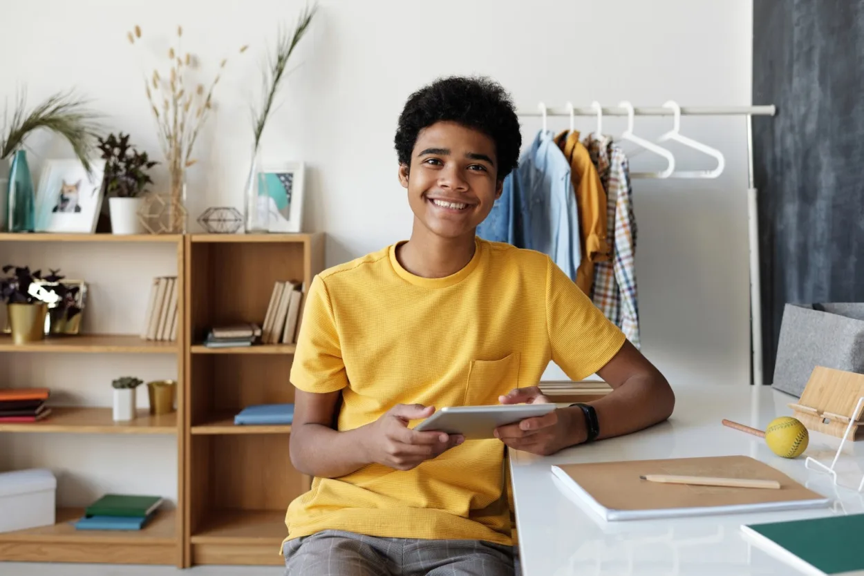 Cheerful teen smiling at the camera with his tablet in his hand