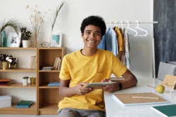 Cheerful teen smiling at the camera with his tablet in his hand