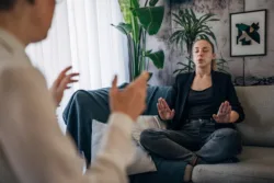 In a serene setting, one individual guides another through a calming breathing technique, fostering an atmosphere of peace and relaxation. The focused expressions and harmonious environment underscore the therapeutic nature of the exercise.