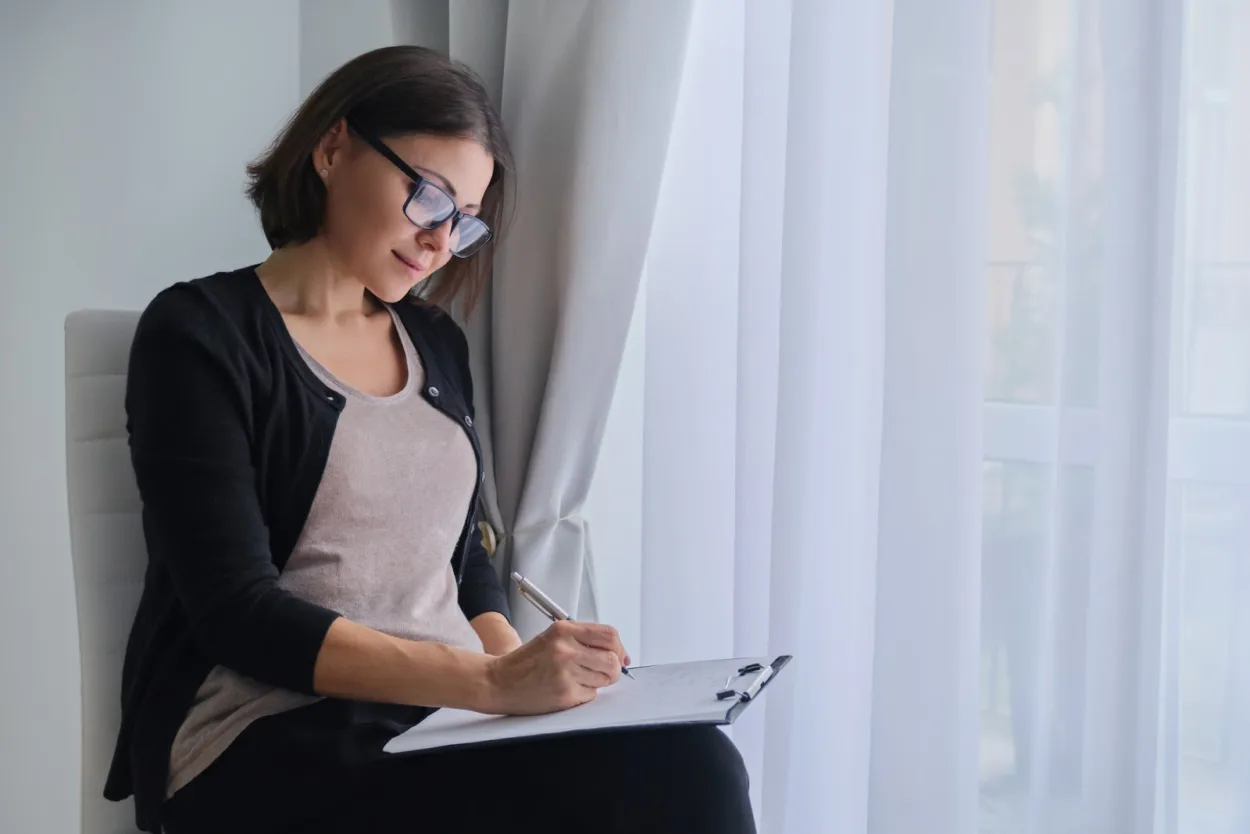 Woman sitting down filling out a list on a clipboard