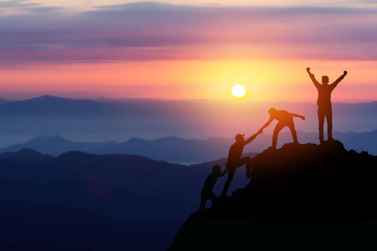 Hikers helping each other climb to the top of a mountain
