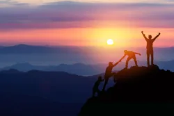 iStock-1255203350 Hikers helping each other climb to the top of a mountain