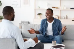 Successful Therapy. Cheerful black man talking to psychologist on meeting at his office, sharing his progress with doctor