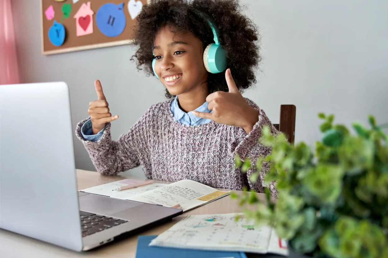 Smiling african mute dumb child school girl learning online class on laptop communicating with teacher by video conference call using sign language showing play hand gesture on virtual therapy lesson.