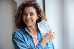 iStock-1285873601 Young adult female smiling while pulling her mask away from her face