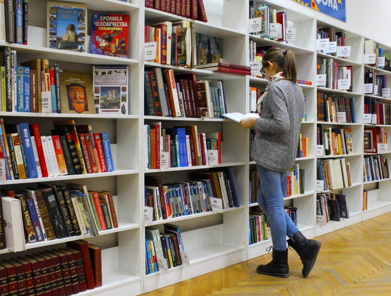 woman reading book from bookshelf