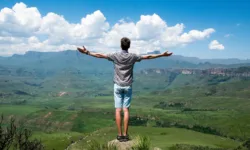 Man Standing on a rock overlooking a valley with his arms spread wide