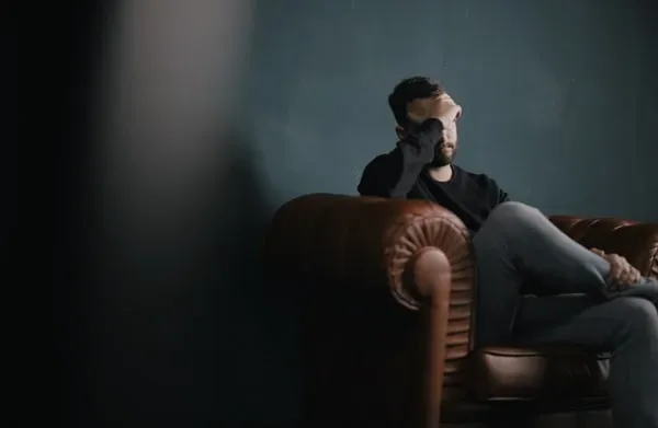man covering face with hands sitting on couch