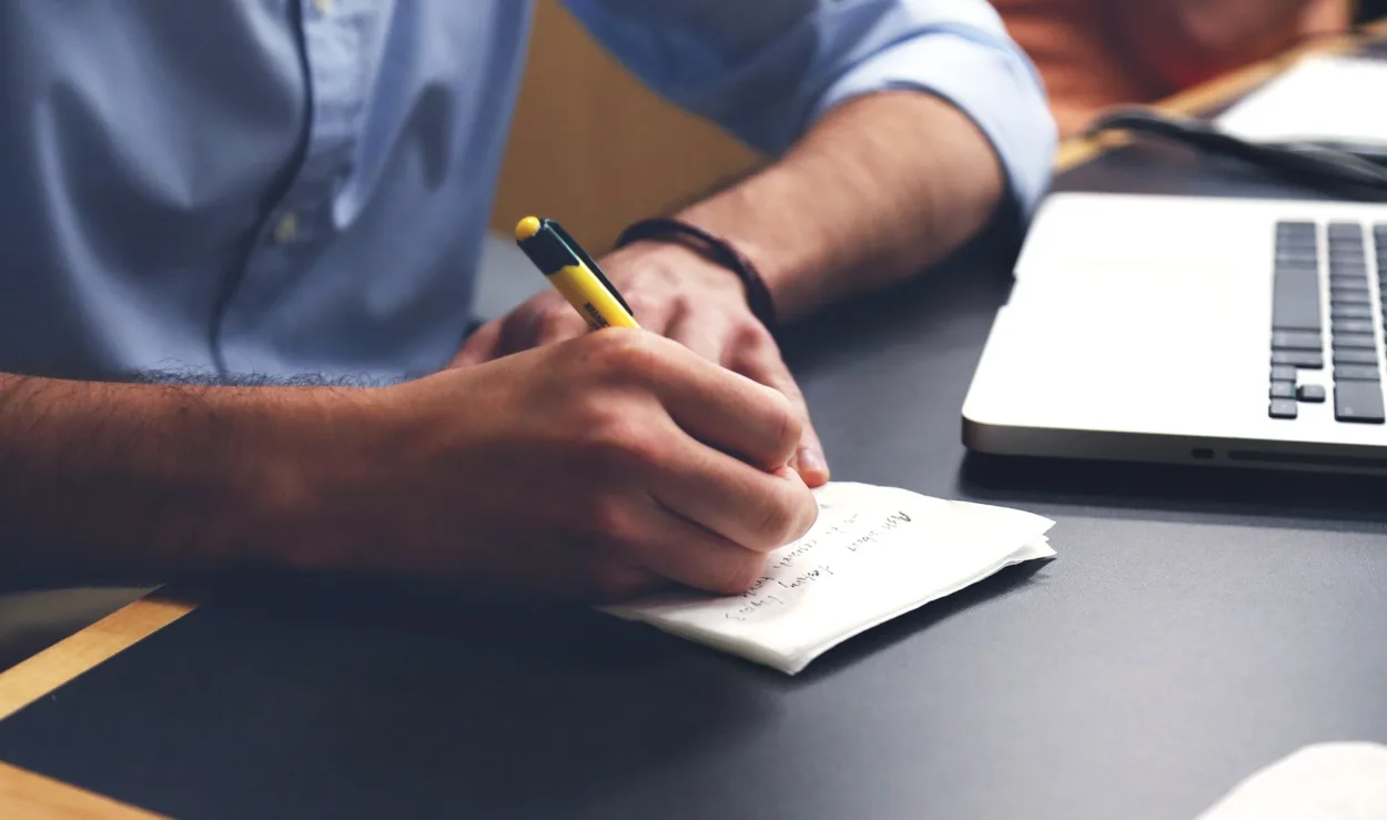 man writing notes from laptop