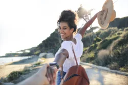 Young woman enjoying her vacation at the sea -Woman walking on a path by the beach, holding a friend's hand - Concept of freedom enjoyment