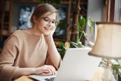 A young woman uses her laptop to participate in a teletherapy session from home with her therapist.