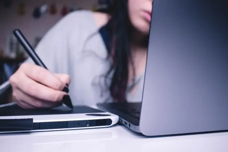 woman writing as she looks as computer