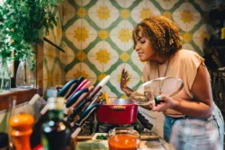 Woman smiling in early recovery with her eyes closed while smelling food cooking in a pot on a stove in her kitchen at home doing what she can to get healthy