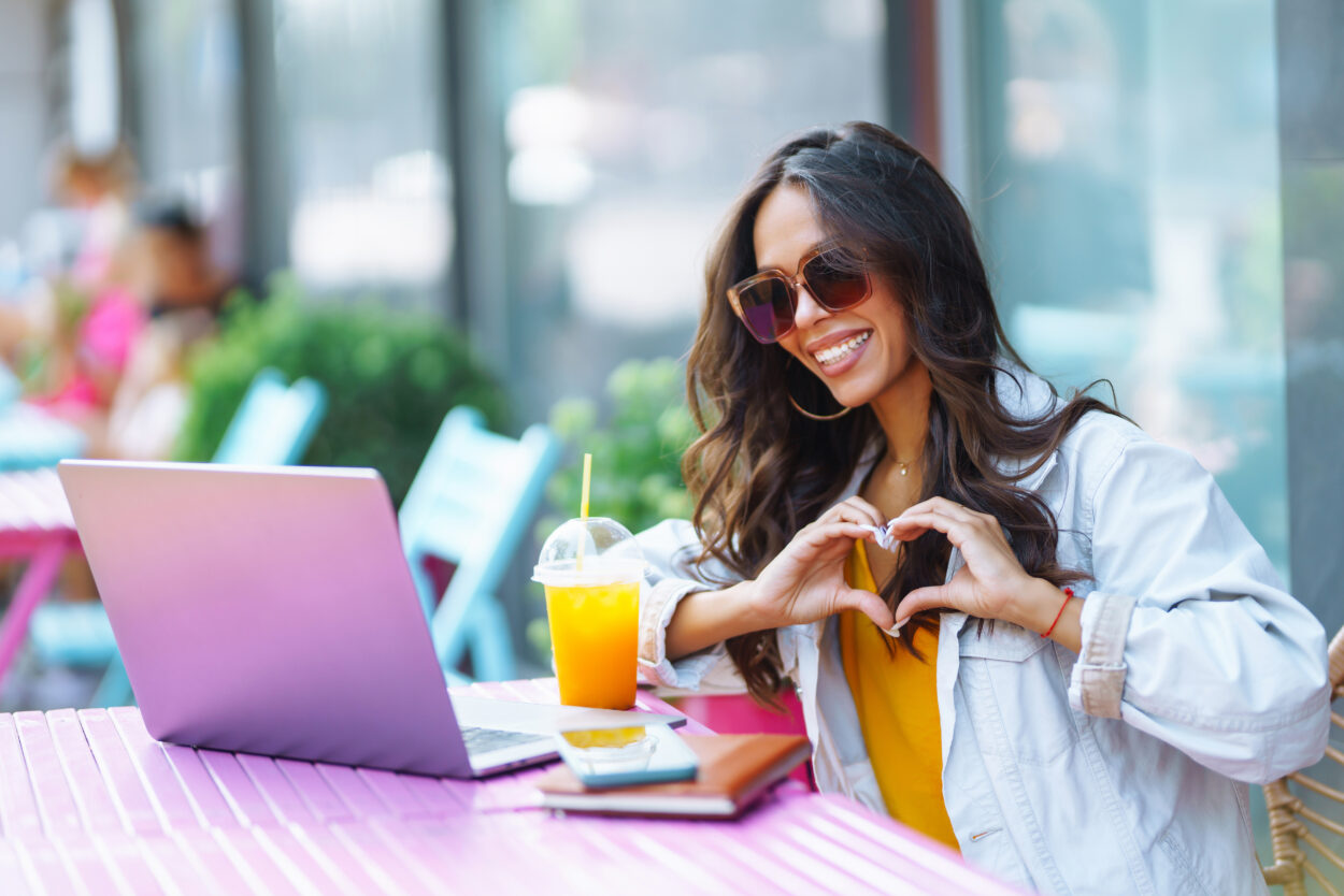 Young woman with wireless headphones calling on laptop, talk by webcam. Freelancer working.